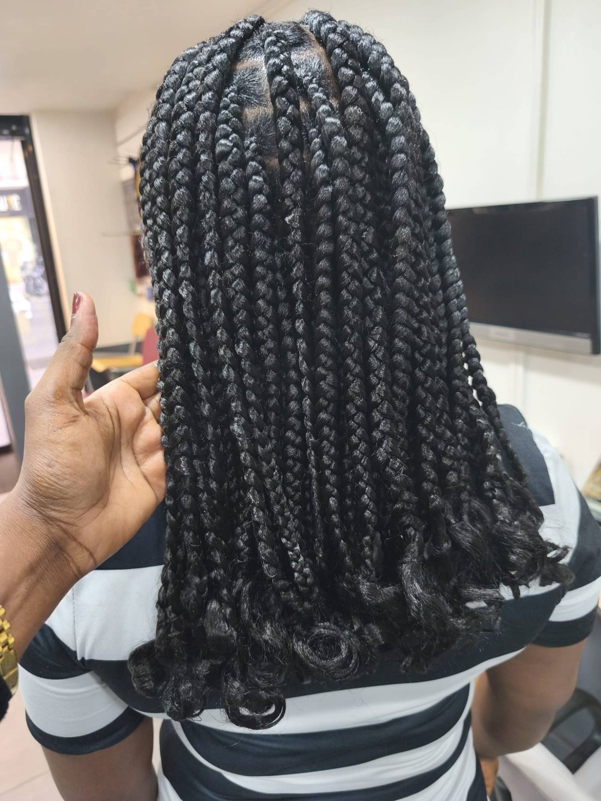 Box braids noires mi-longues aux pointes bouclées, vues de dos au salon.